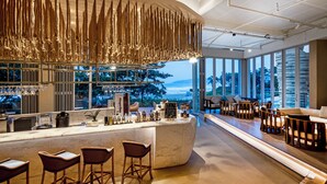 Zona de bar moderna con una barra curva, taburetes de mimbre y vistas al océano.