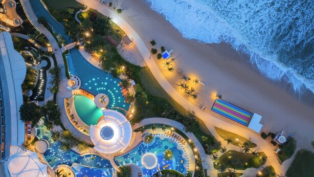 Vista aérea de un resort con una piscina grande, un tobogán acuático y una zona de playa.