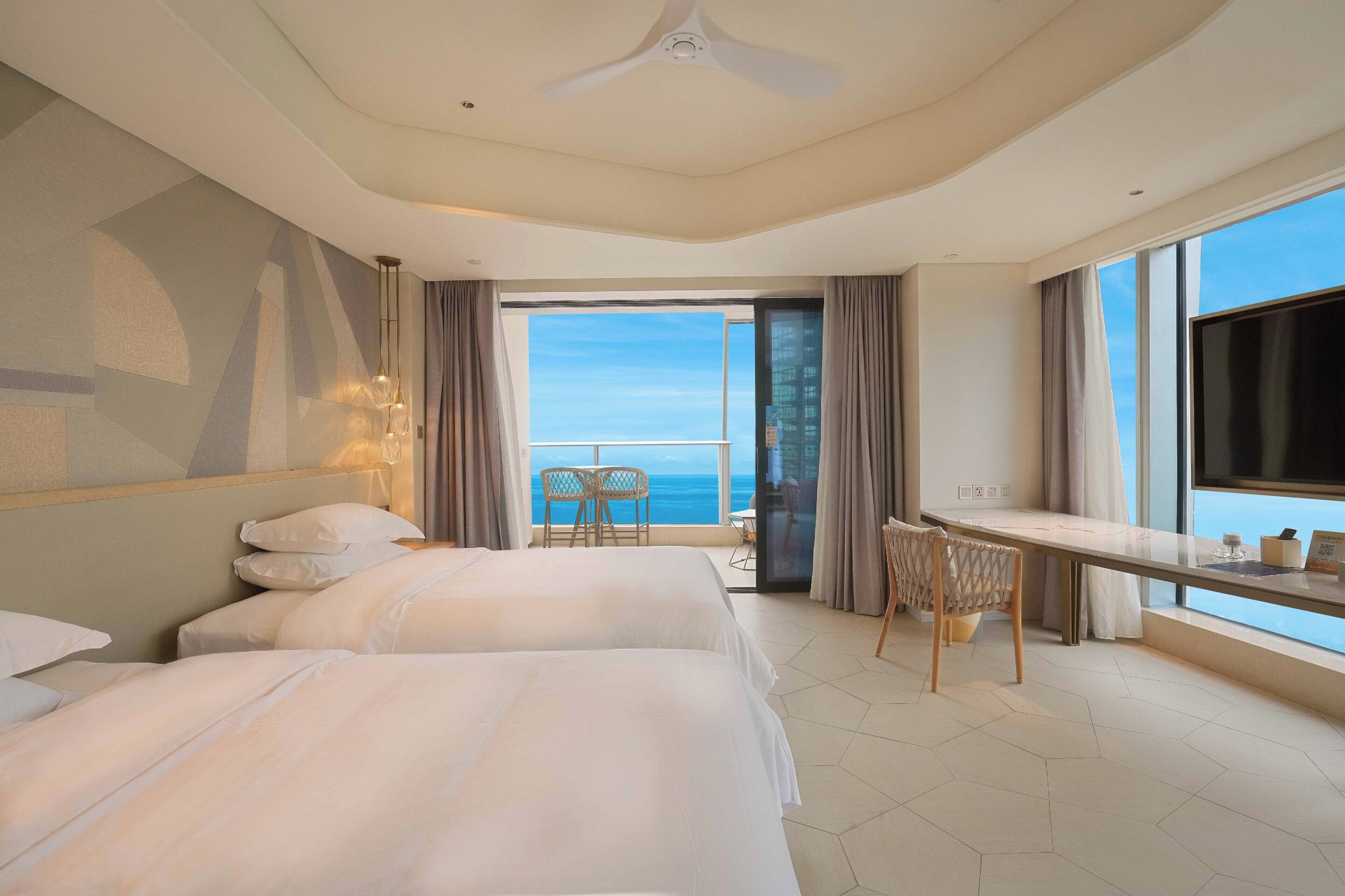 Habitación de hotel con dos camas, una mesa de comedor, televisión y balcón con vista al mar.