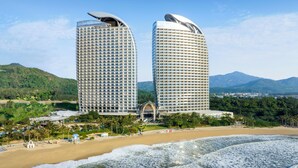 Dos hoteles altos con una playa y montañas al fondo.