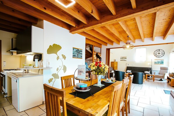 Un vaste espace de vie doté d’un plafond en bois, d’une table à manger avec des chaises, d’un coin cuisine et d’un canapé.