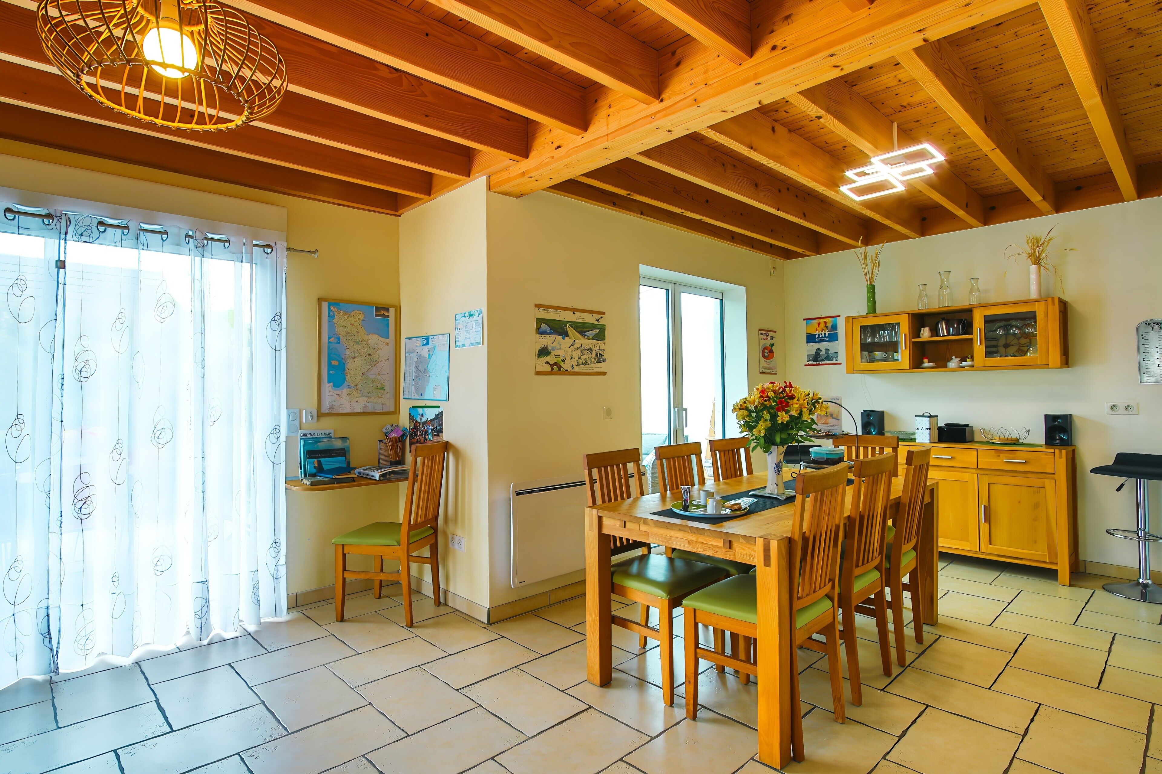 A dining area with a wooden table and chairs, a kitchen with cabinets, and a ceiling with exposed beams.