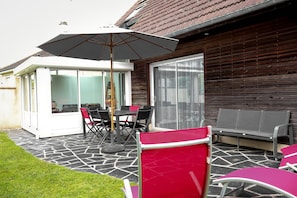Une terrasse avec une table et des chaises, une chaise rouge, un banc gris et un parasol blanc.