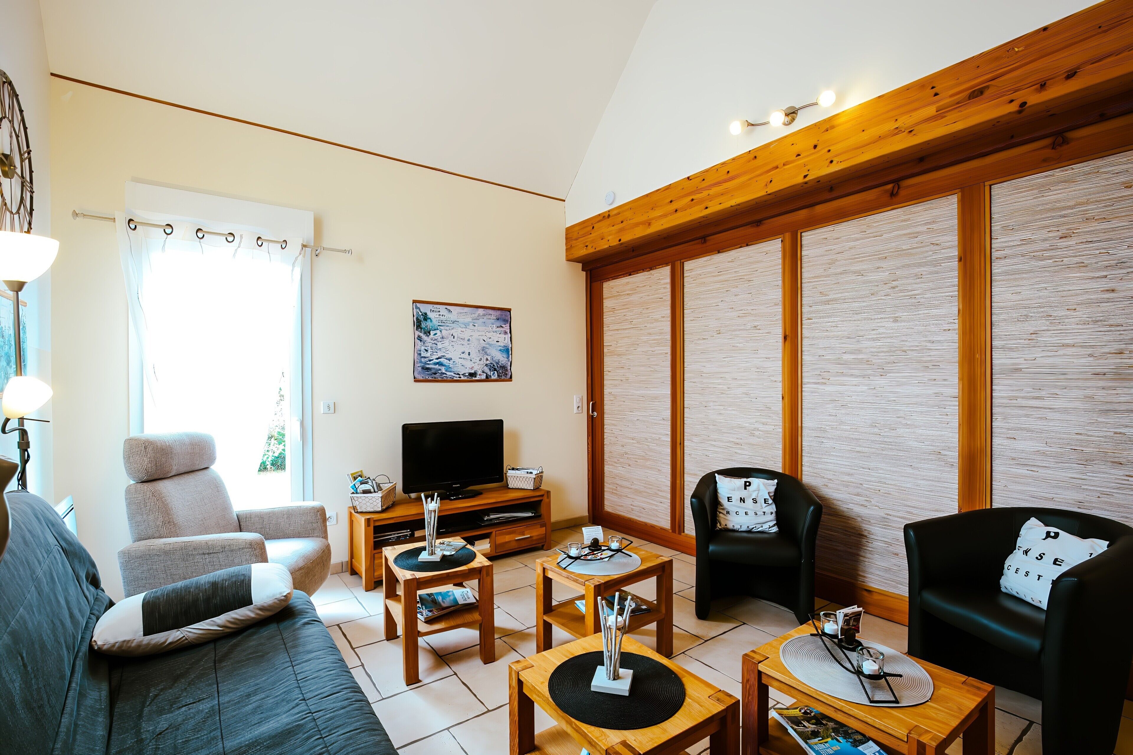 Een woonkamer met een bank, twee fauteuils, een salontafel, een televisie en een houten plafond.