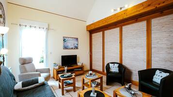 Een woonkamer met een bank, twee fauteuils, een salontafel, een televisie en een houten plafond.