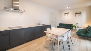 A modern kitchen with a central island, dark cabinets, and a green sofa in a living area. - Opera Square Family Apartment for 10 Guests (Antwerp)