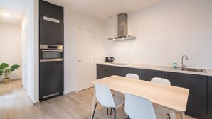 A modern kitchen with a built-in oven, a stainless steel range hood, and a dining area with a wooden table and white chairs. - Opera Square Family Apartment for 10 Guests (Antwerp)
