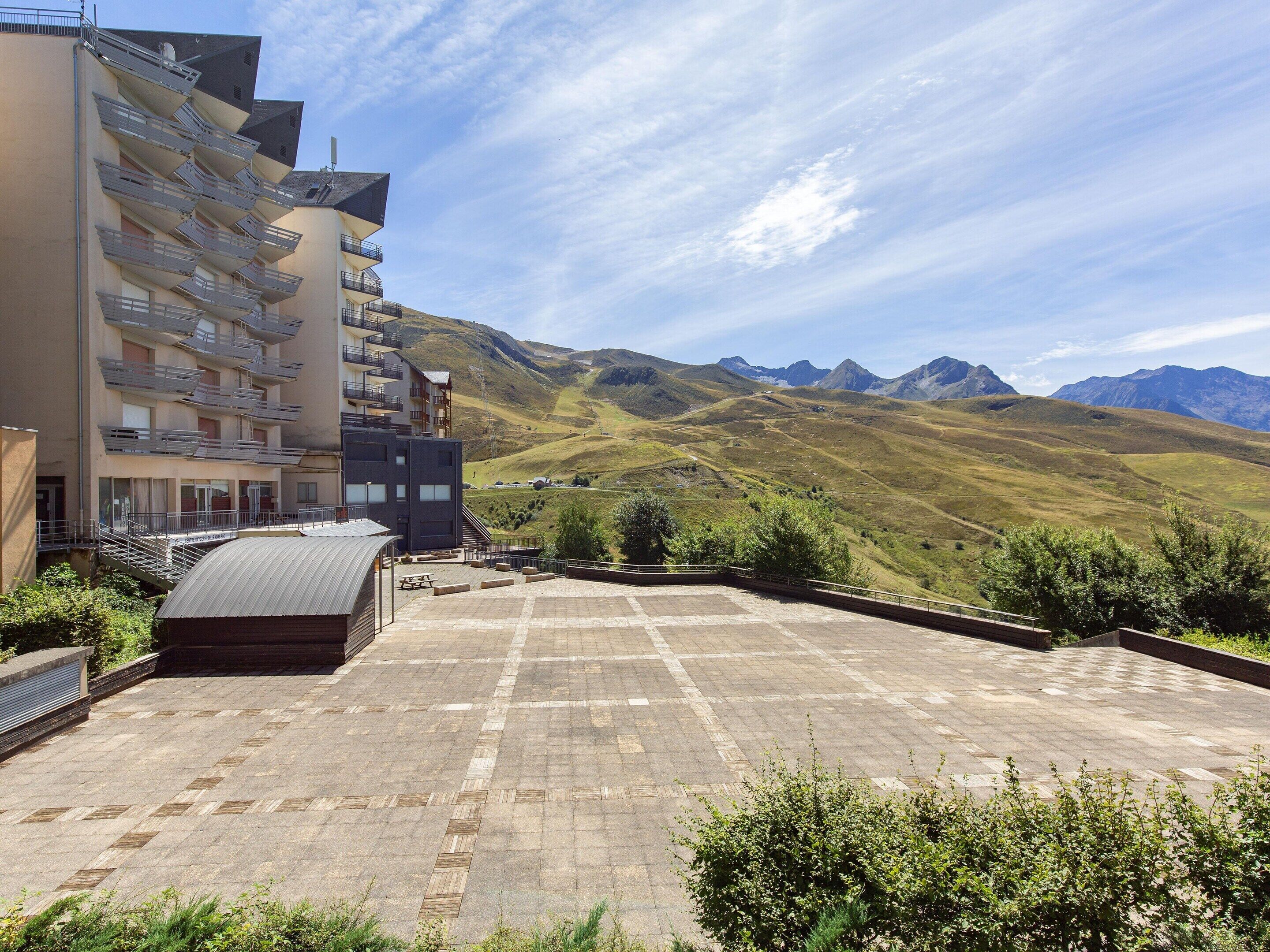 A building with multiple balconies, a flat roof terrace, and a mountainous landscape in the background.