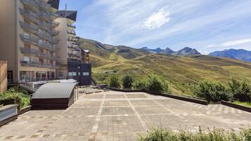 A building with multiple balconies, a flat roof terrace, and a mountainous landscape in the background.