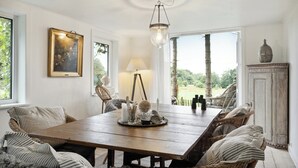 A dining room with a wooden table, wicker chairs, a chandelier, and a view of the outdoors. - Nature-close home near beach at Limfjorden (Thyholm)