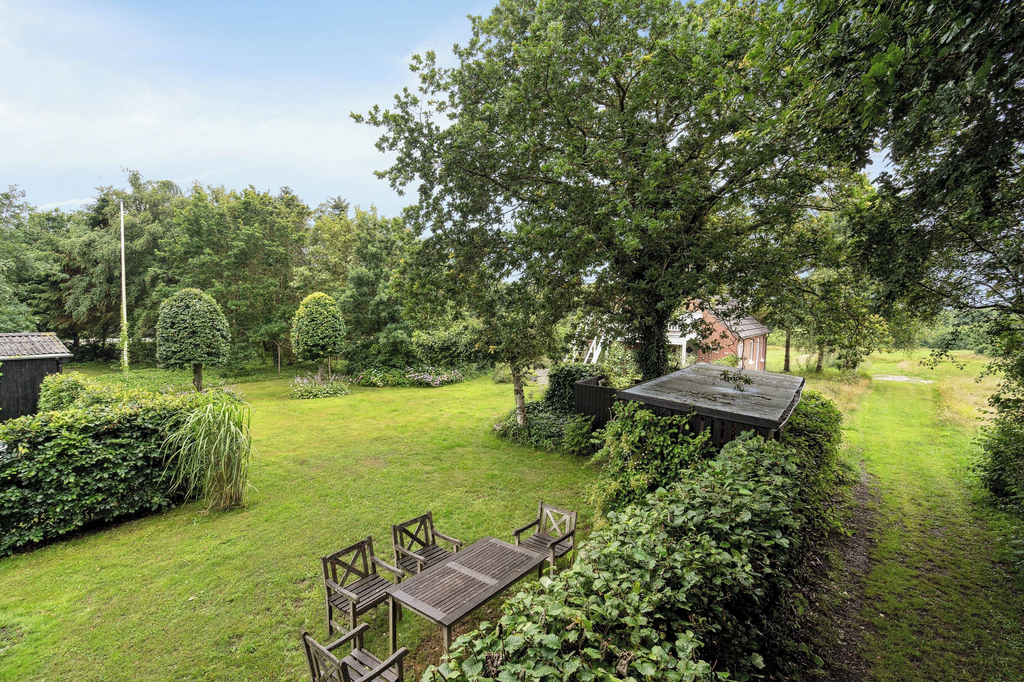 A well-maintained garden with a wooden table and chairs, surrounded by lush greenery and trees.