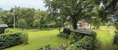 A well-maintained garden with a wooden table and chairs, surrounded by lush greenery and trees.