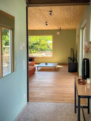 Un interior modern amb sostre de fusta, zona de menjador, sofà i vista a la vegetació exterior.