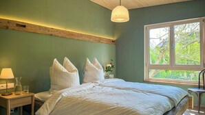 Une chambre à coucher comprenant un lit, une table de chevet, une lampe, une fenêtre donnant sur un paysage verdoyant et un plafond en bois.
