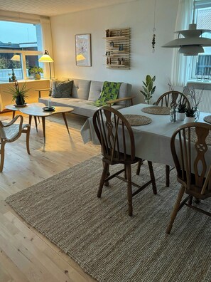 Een moderne woonkamer met een eethoek, houten meubels, een bank, een tafel en een groot raam.