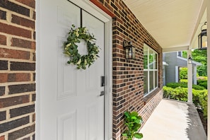 A brick house with a white door, a wreath, and a small plant on the porch. - Urban Oasis in Charotte (Charlotte)