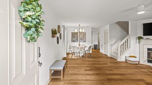 A hallway with a wooden floor, a bench, a dining area with chairs, a staircase, and a fireplace. - Urban Oasis in Charotte (Charlotte)