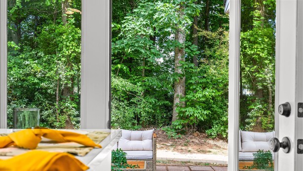 A room with a view of a lush garden through glass doors, a wicker sofa, and a patterned rug. - Urban Oasis in Charotte (Charlotte)