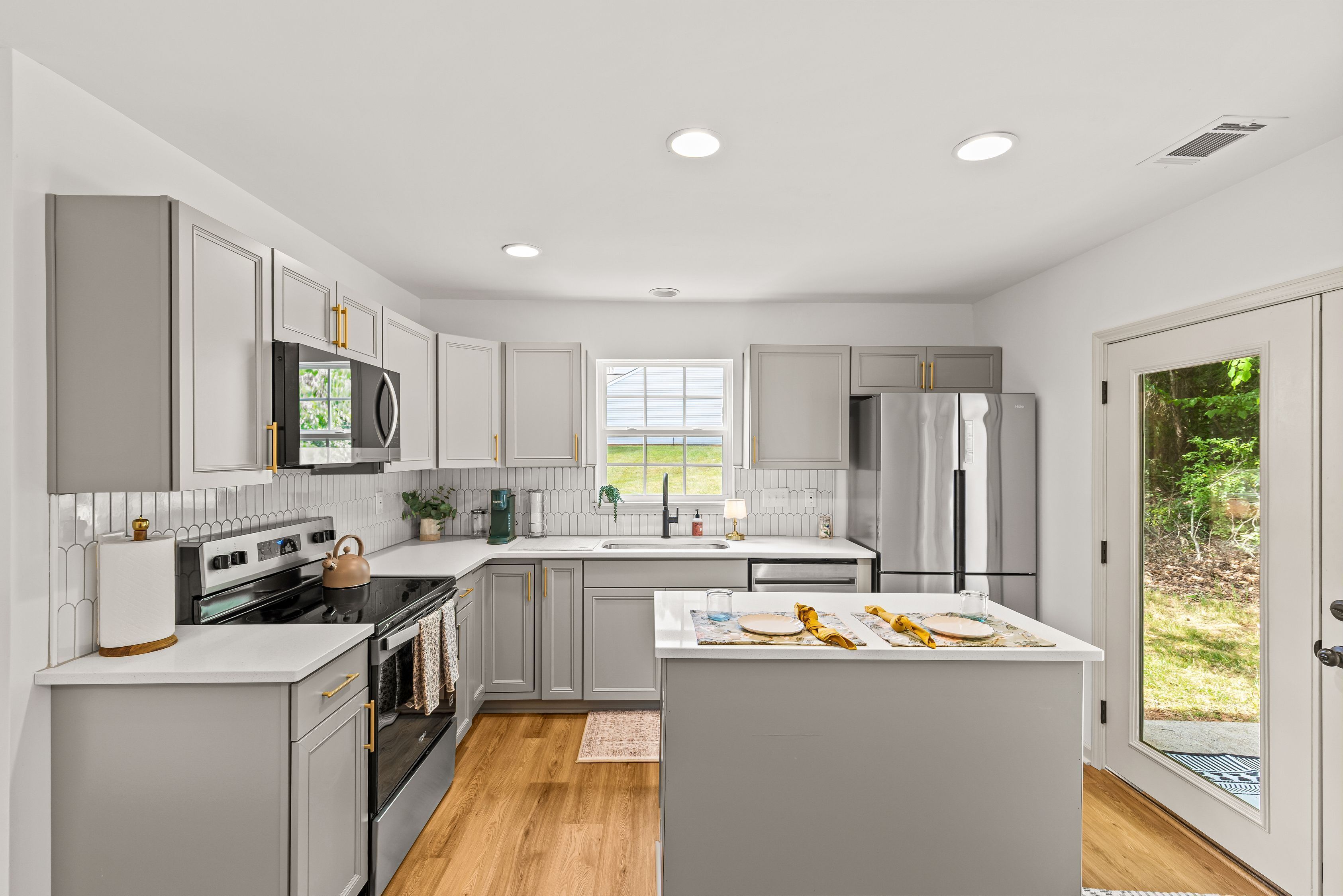 A modern kitchen with grey cabinets, a central island, and a window providing a view of the outdoors.