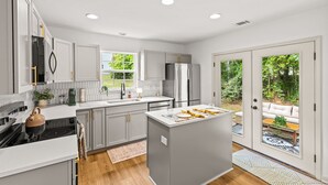 A modern kitchen with a central island, stainless steel appliances, and a view of a garden through glass doors. - Urban Oasis in Charotte (Charlotte)