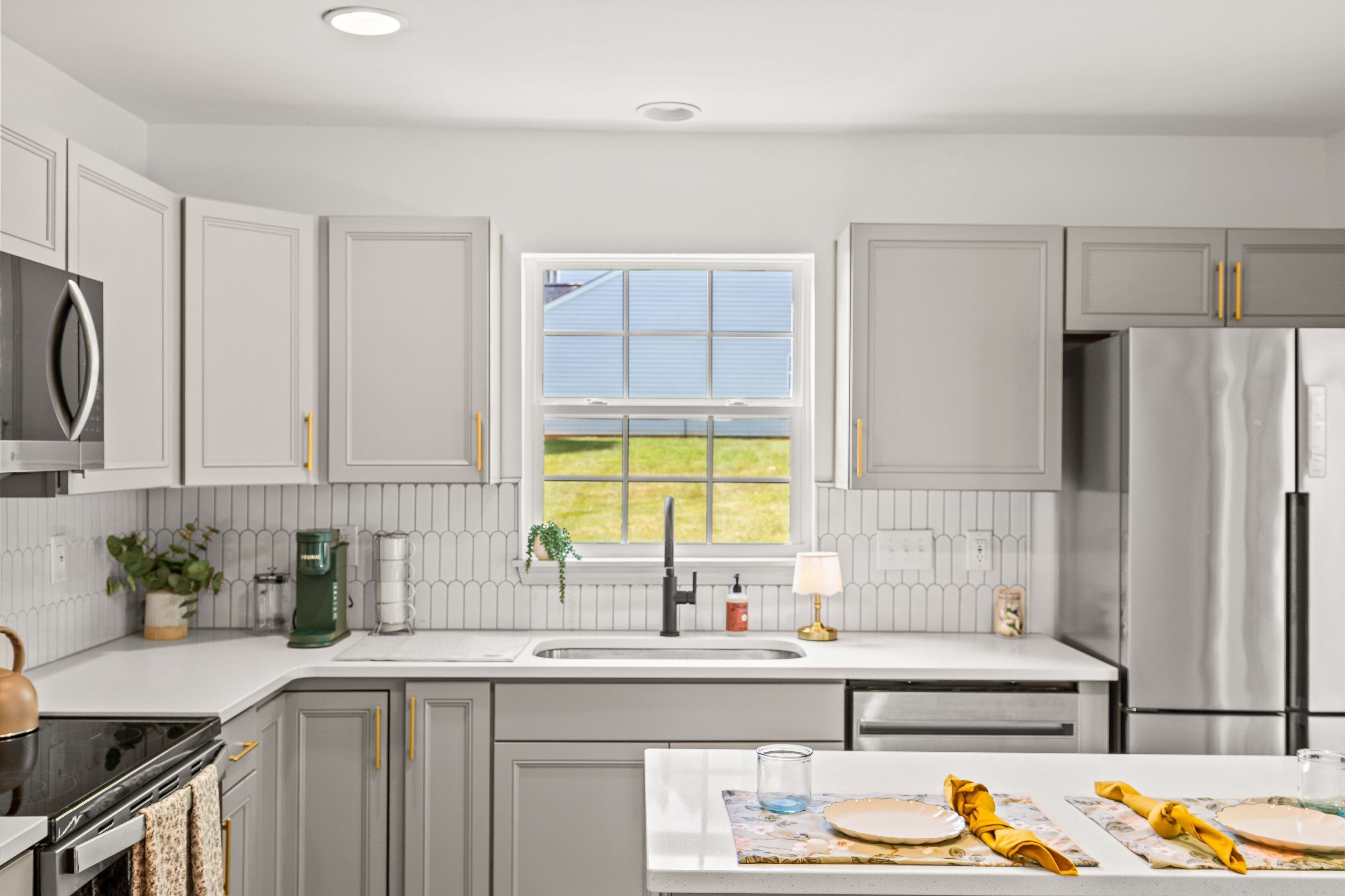 A modern kitchen with grey cabinets, a stainless steel refrigerator, a window with a view of the outdoors, and a dining area set with plates and napkins.