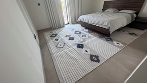 A bedroom with a bed, a patterned rug, and a wooden headboard.
