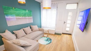 En stue med sofa, rundt tæppe, fladskærms-tv og et vindue med gardiner.