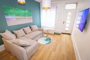 Ein Wohnzimmer mit einer Couch, einem runden Teppich, einem Flachbildfernseher und einem Fenster mit Vorhängen.