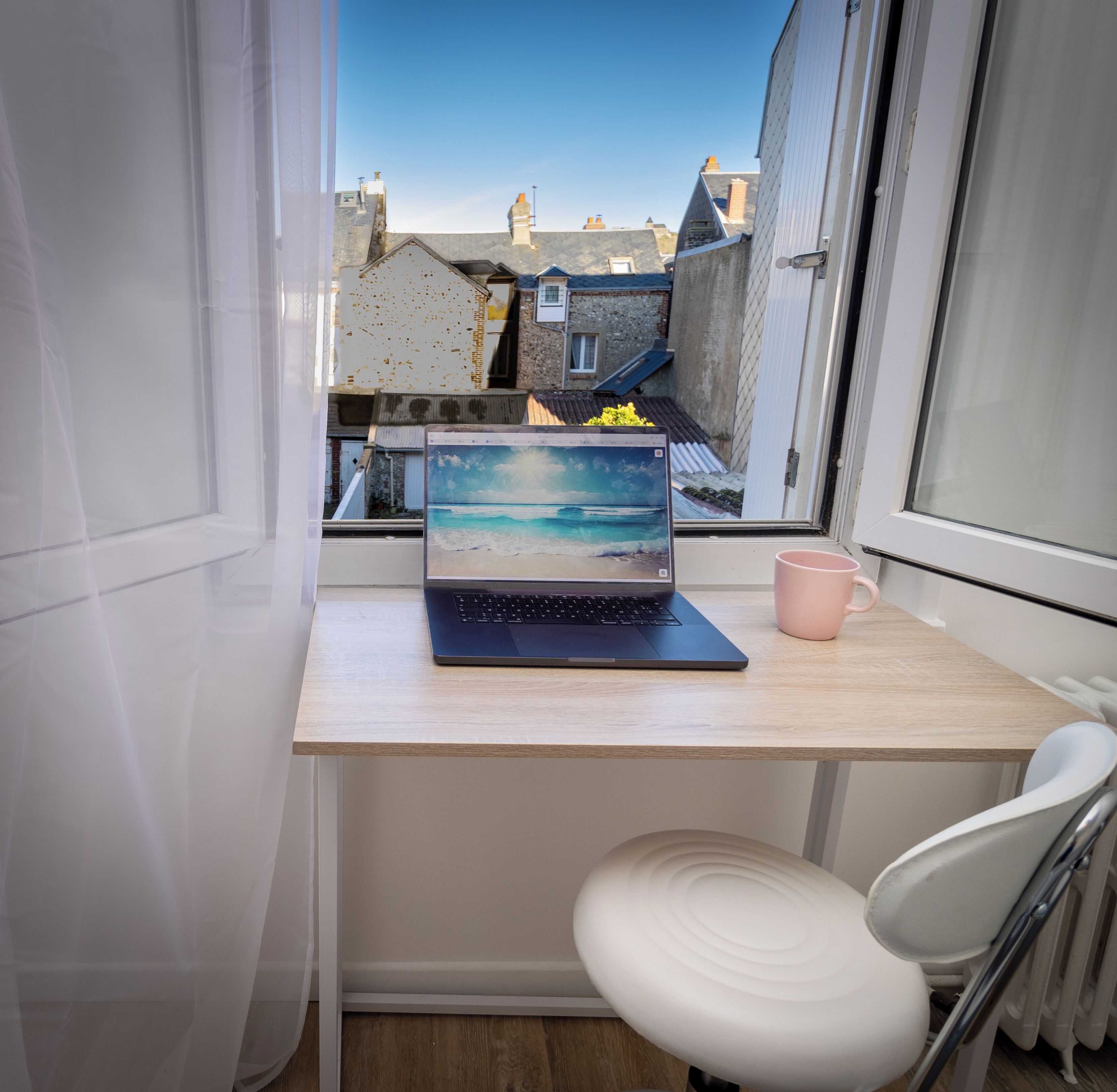 Een laptop op een bureau met uitzicht op gebouwen door een raam.