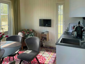 A compact living space with a kitchenette, a flat-screen TV, a dining table with chairs, and a patterned rug. - Cottage near golf course and nature reserve in När (Stånga)