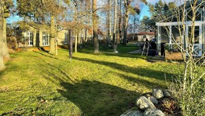 A residential property with a grassy yard, trees, and a house with a red roof.