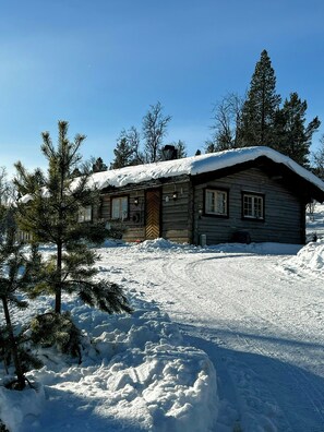 Eine Blockhütte mit schneebedecktem Dach, umgeben von Schnee und Kiefern.