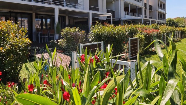 Ein mehrstöckiges Hotel mit Balkonen, einem Garten mit verschiedenen Pflanzen und blauem Himmel.
