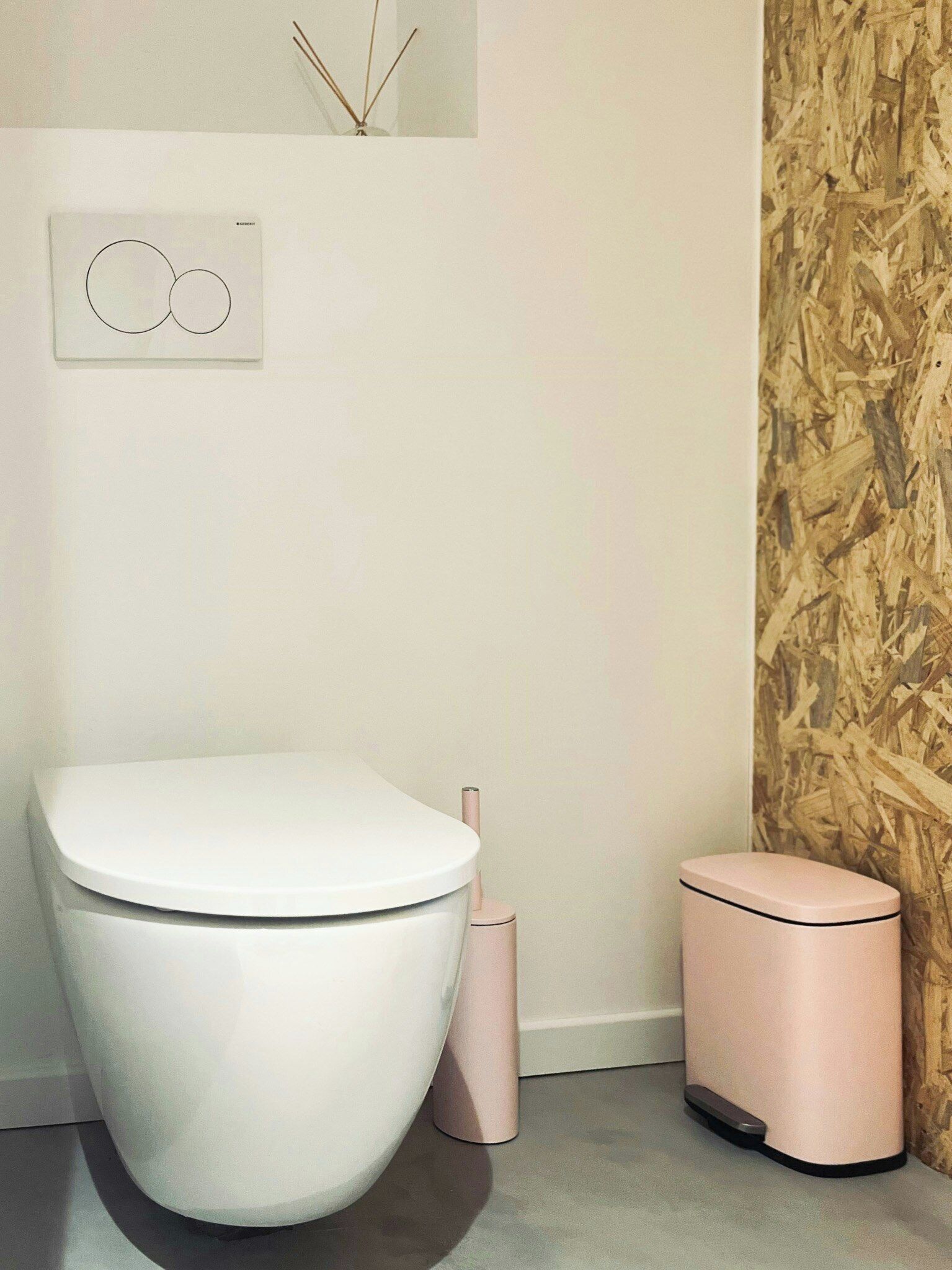 Ein modernes Badezimmer mit Toilette in Weiß, einem rosa Bidet und einem an der Wand befestigten Toilettenpapierhalter.