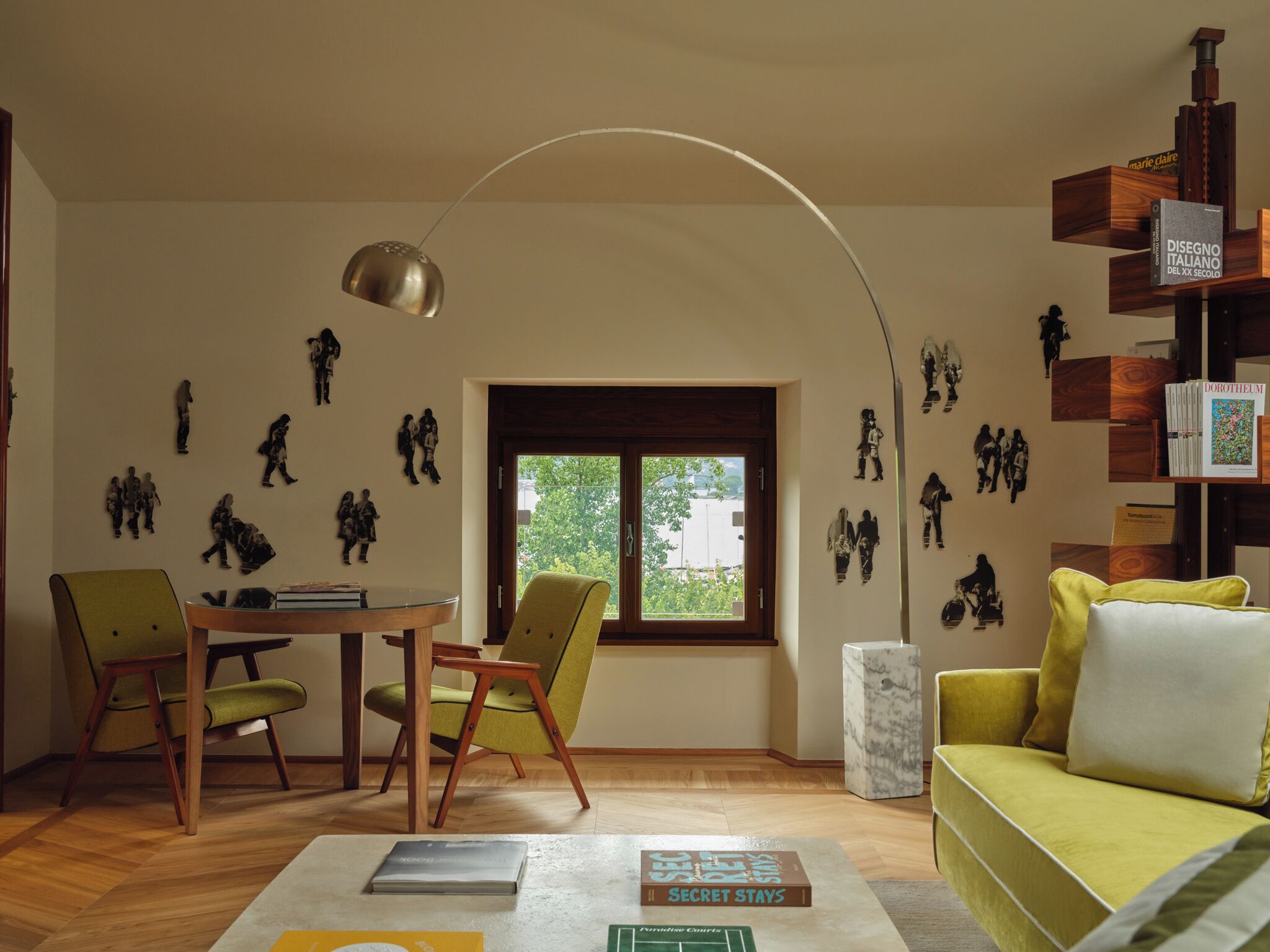 A living room with a sofa, chairs, a table, a bookshelf, and a window with a view.