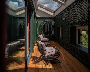 A covered outdoor area with wooden flooring, green lattice walls, and two chairs.
