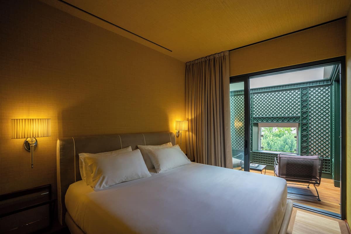 Habitación de hotel con una cama grande, dos lámparas de noche, una ventana y vistas a zonas verdes.