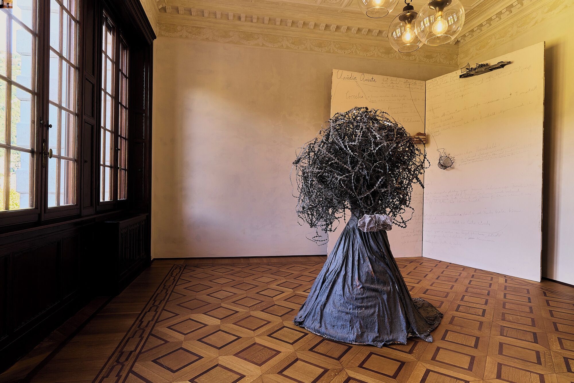 A room with a large window, a patterned wooden floor, and a sculpture on the wall.
