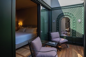 A bedroom with a bed, two chairs, a small table, and a decorative mirror.