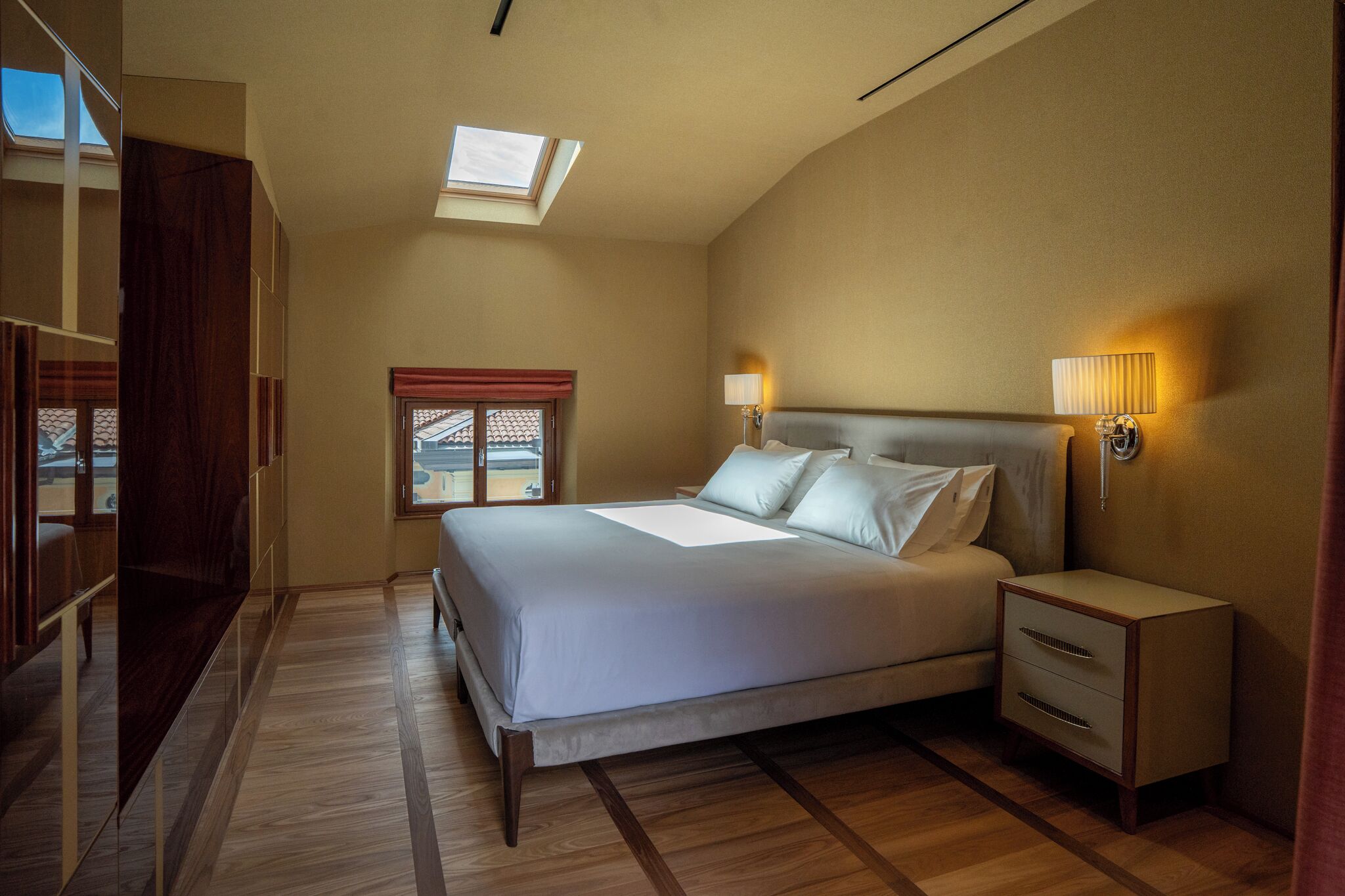 A bedroom with a bed, bedside lamps, a nightstand, a window with a view, and a skylight.