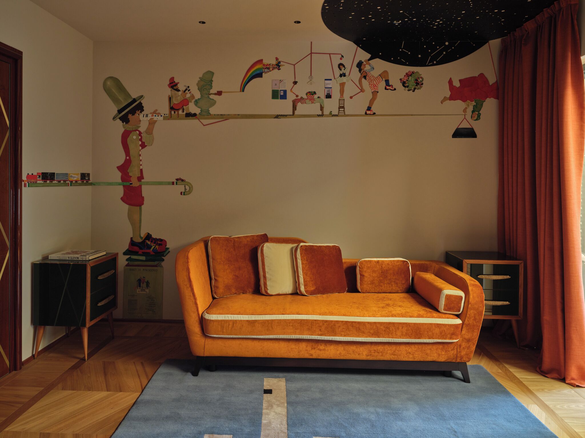 A retro-themed living room with a vintage orange sofa, a small side table, a bookshelf, and a wall mural.