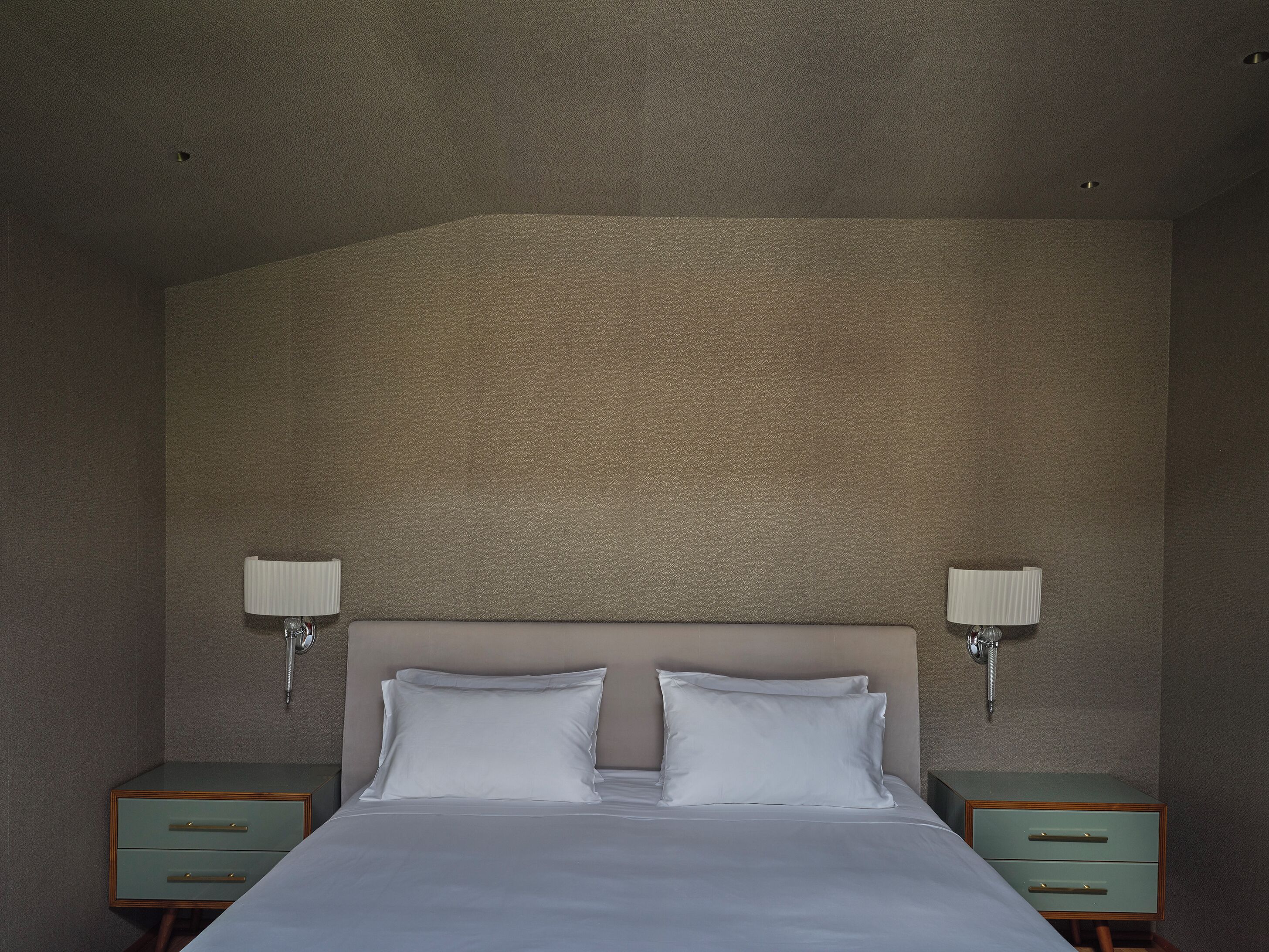 A hotel room with a large bed, two bedside tables, and wall-mounted lamps.