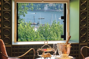 A window view of a harbor with boats, a balcony with a table set for a meal, and a champagne bucket.
