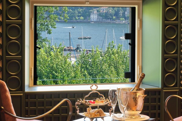 A window view of a harbor with boats, a balcony with a table set for a meal, and a champagne bucket.