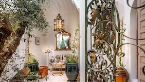A room with a large tree trunk, potted plants, a chandelier, and a mirror. - Riad Anaqa (Marrakech)