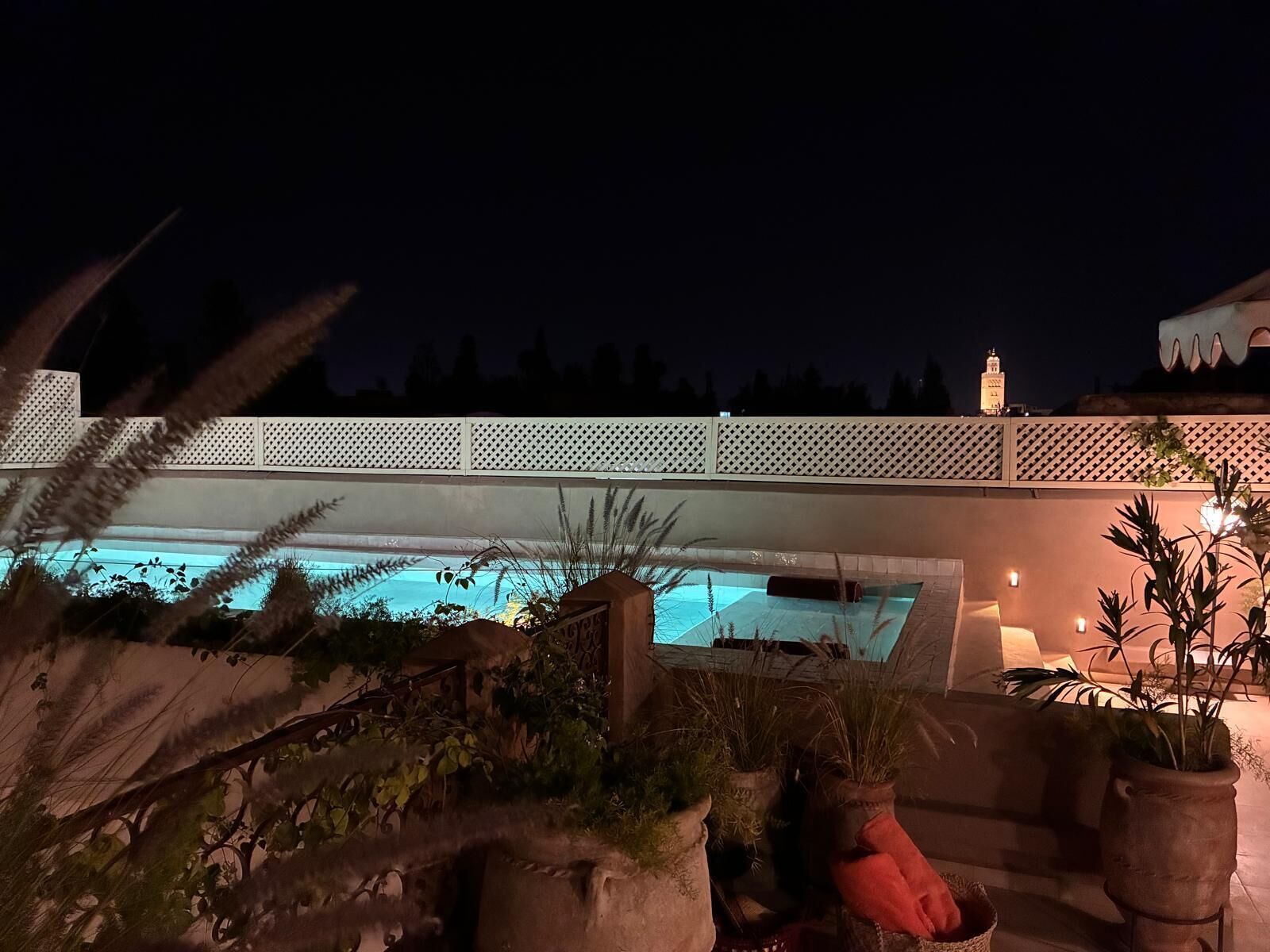 A pool area with a white fence, potted plants, and a view of a building with a tower.