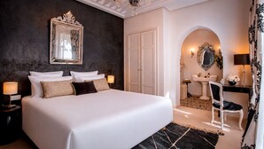 A bedroom with a large bed, a chandelier, a mirror, and a bathroom with a sink and chair. - Riad Anaqa (Marrakech)