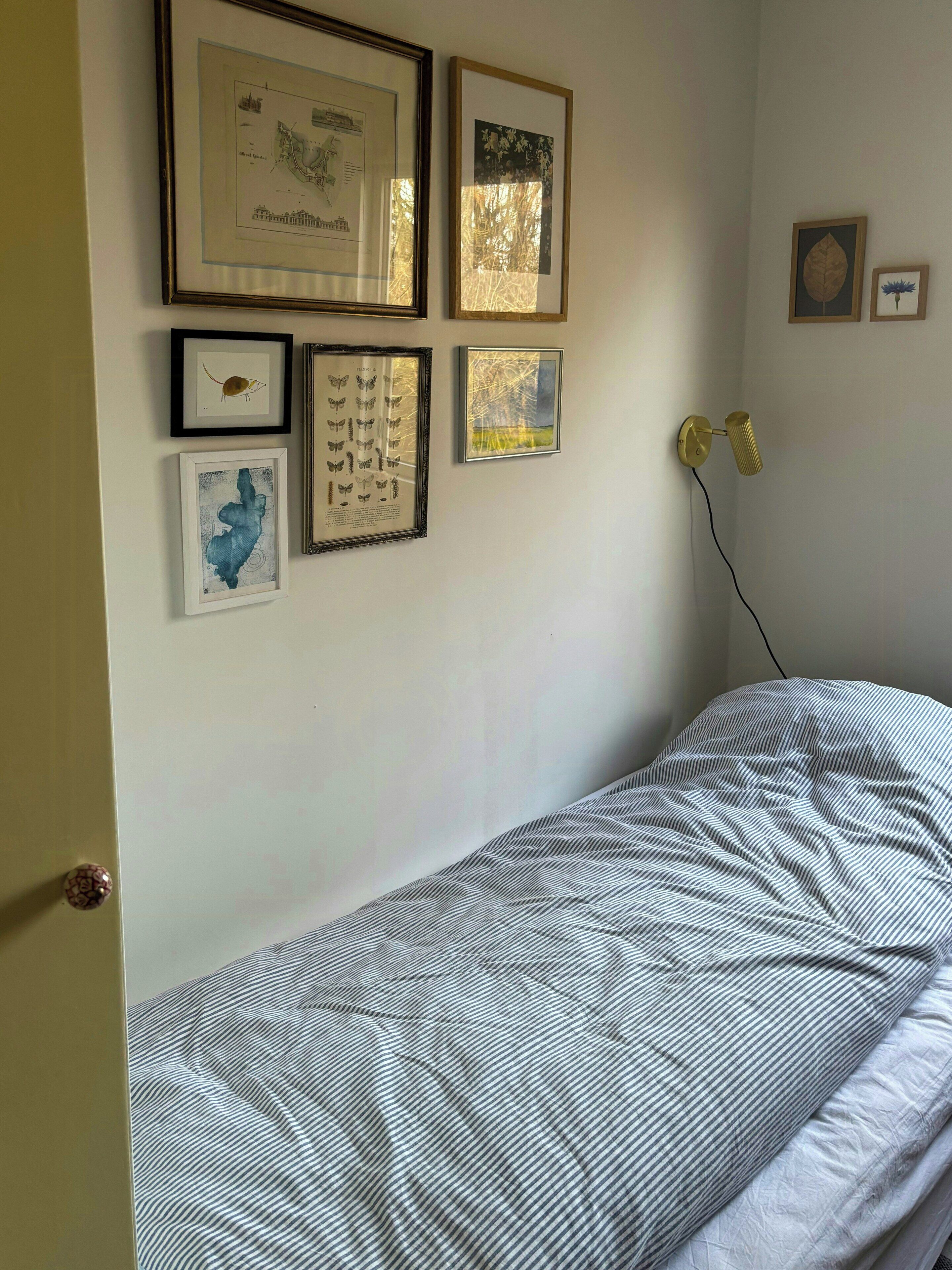 Une chambre à coucher avec un lit, une lampe fixée au mur et des tableaux encadrés.
