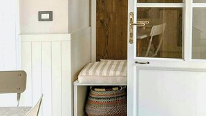 Una habitación con puerta de madera, un banco, una cesta y un estante de pared con objetos decorativos.