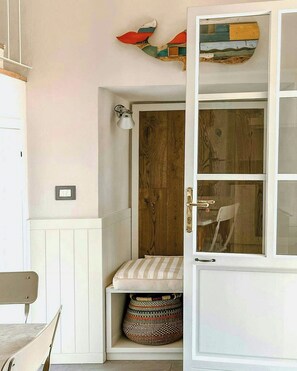Ein Zimmer mit Holztür, einer Bank, einem Korb und einem an der Wand befestigten Regal mit Dekoration.